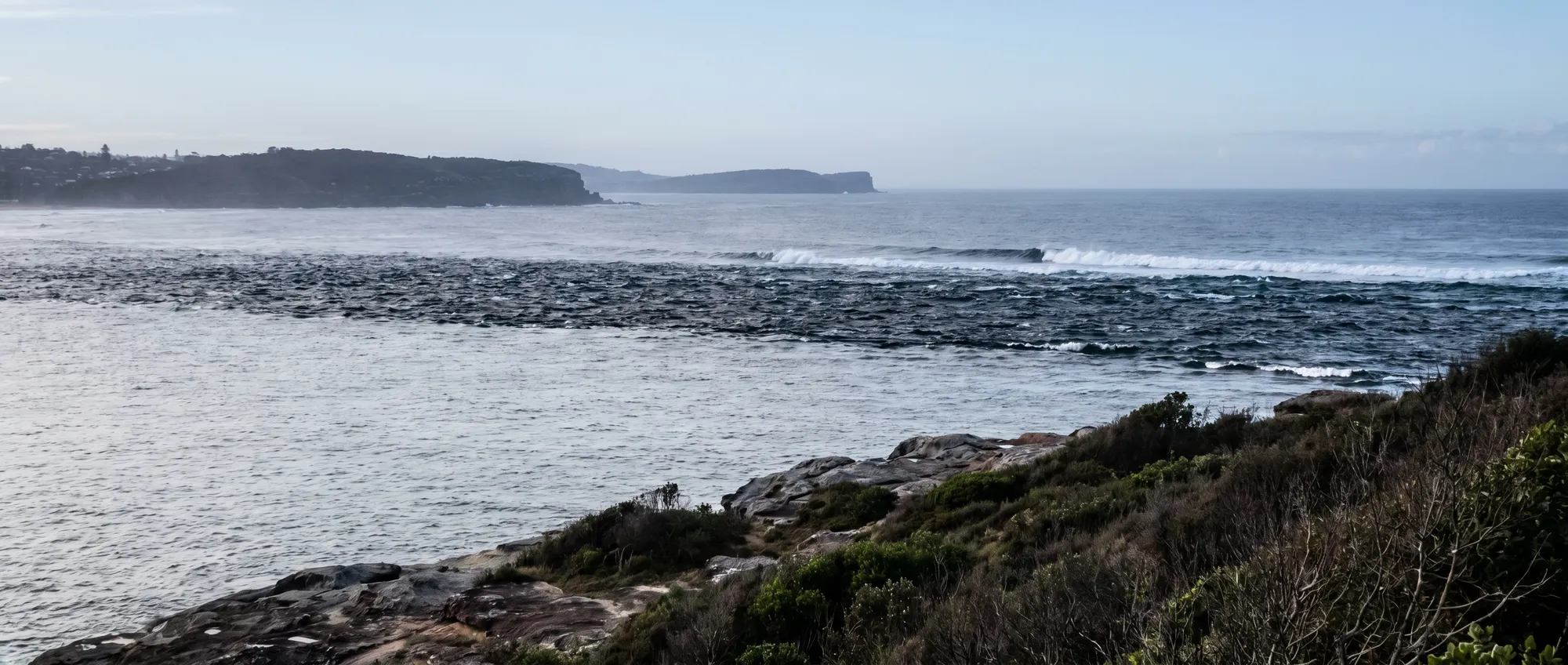The dark ruffled line of a southerly wind change advancing over glassy sea off a Northern Beaches headland